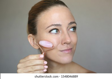 Beautiful Woman Using Pink Jade Rose Quartz Facial Roller. Skin Treatment.