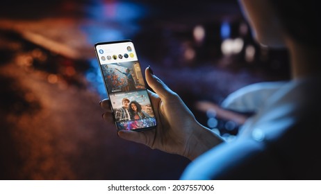 Beautiful Woman is Using Smartphone, Checking Social Media News Feed Full of Newly Posted Photos. Anonymous Female Walking Through Night City Street Full of Neon Light. View of a Phone Screen - Powered by Shutterstock