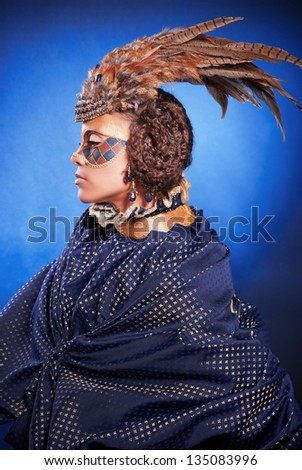Beautiful woman in venetian mask with feathers and jewelry, in a suit of blue color on a blue background.