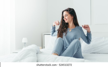 Beautiful woman waking up in her bed in the bedroom, she is stretching and smiling