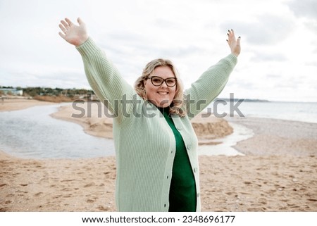 Beautiful woman walking in the sand beach in cold weather. Overweight model have fun . The happy girl wearing knit polluver. The plus size girl raised her hands up