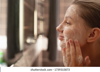 A Beautiful Woman Washes Her Skin On Her Face In The Bathroom By The Mirror. Side View . Healthy Facial Skin. Skin Care. Pore Cleansing.
