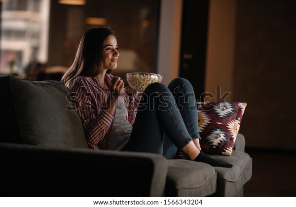 Beautiful woman watching movie in the night\
sitting on a couch in the living room at\
home