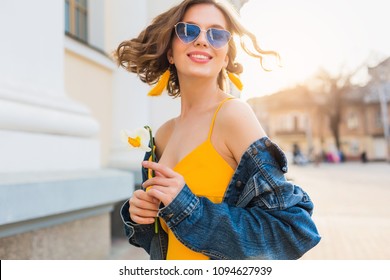 beautiful woman waving hair smiling, stylish apparel, wearing denim jacket and yellow top, fashion trend, summer style, happy positive mood, sunny day, sunrise, street fashion, blue sunglasses