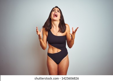 Beautiful Woman Wearing Bikini Swimwear Over White Isolated Background Crazy And Mad Shouting And Yelling With Aggressive Expression And Arms Raised. Frustration Concept.