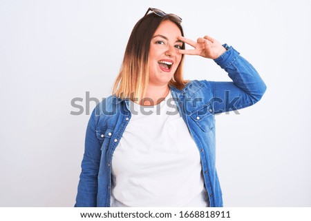 Beautiful woman wearing denim shirt standing over isolated white background Doing peace symbol with fingers over face, smiling cheerful showing victory