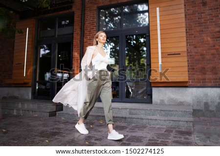 Beautiful Woman Wearing Fashionable Spring, Fall Clothes (beige trench coat, oversize khaki cargo pants, accessorie) Outdoors. Female stylish Model walking city Street. Autumn trend, fashion outfit