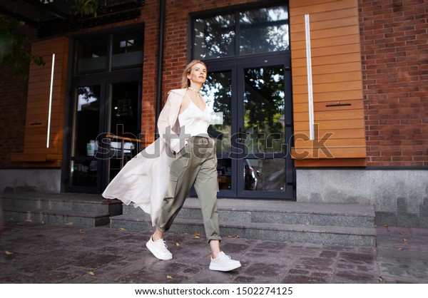 Beautiful Woman Wearing Fashionable Spring, Fall\
Clothes (beige trench coat, oversize khaki cargo pants, accessorie)\
Outdoors. Female stylish Model walking city Street. Autumn trend,\
fashion outfit