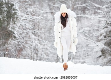 Beautiful Woman Wearing Fashionable Winter Clothes (white down jacket, knitted stylish hat, sweater, leggings, mittens, felt boots) Outdoors. Female stylish Model walking in winter nature