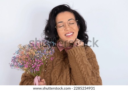 beautiful woman wearing knitted sweater over white background grins joyfully, imagines something pleasant, copy space. Pleasant emotions concept.