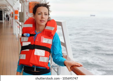 Beautiful Woman Wearing In Orange Life Jacket Looks Into Distance At Deck Of Ship