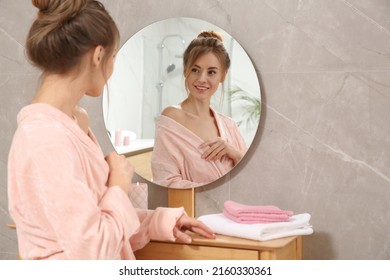 Beautiful woman wearing pink bathrobe in front of mirror at home