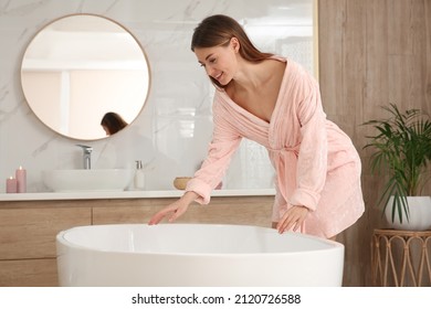 Beautiful woman wearing pink robe near tub in bathroom - Powered by Shutterstock