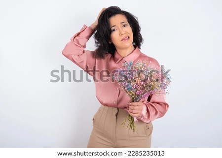 beautiful woman wearing pink shirt over white background being confused and wonders about something. Holding hand on head, uncertain with doubt. Pensive concept.