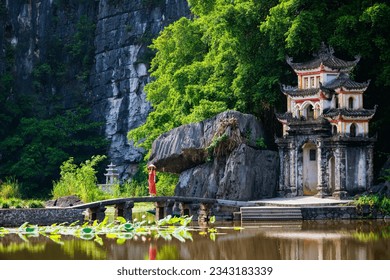 Beautiful woman wearing red dress and conical hat visiting Bich Dong pagoda in Ninh Binh Vietnam. Bich Dong Pagoda is a popular tourist destination of Asia. - Powered by Shutterstock