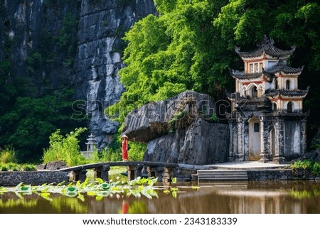 Beautiful woman wearing red dress and conical hat visiting Bich Dong pagoda in Ninh Binh Vietnam. Bich Dong Pagoda is a popular tourist destination of Asia.