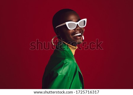 Beautiful woman wearing stylish sunglasses and smiling against red background. African female model wearing funky sunglasses.