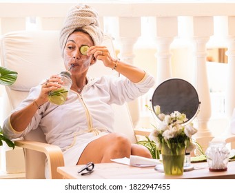 Beautiful Woman Wearing White Bathrobe With Cucumber Skin Care Mask While Drinking Detox Drink. DIY Home Spa