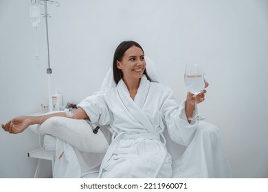 Beautiful Woman In White Bathrobe Drink Water During Medical Procedure In Beauty Clinic