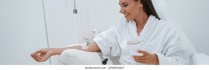 Beautiful woman in white bathrobe drink water during medical procedure in beauty clinic - Powered by Shutterstock