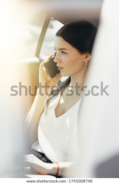 Beautiful woman in a white blouse talking\
with a colleague on the phone and looking out the window from the\
passenger\
compartment.