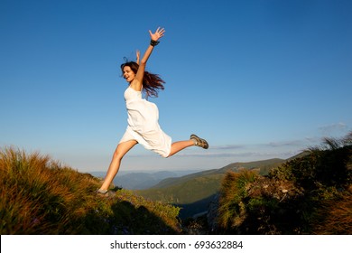 Beautiful woman in white dress running in the mountains. Jumping on mountain peak rock. Beautiful girl looking happy and smiling. Relaxing, feeling alive, breathing fresh air, got freedom from work - Shutterstock ID 693632884
