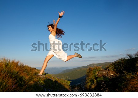 Beautiful woman in white dress running in the mountains. Jumping on mountain peak rock. Beautiful girl looking happy and smiling. Relaxing, feeling alive, breathing fresh air, got freedom from work
