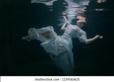 Beautiful woman in a white dress swims under the water.