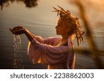 A beautiful woman in a white dress with a wreath on her head stands in the water. Slavic girl bathes in the lake at sunset. Ivana Kupala