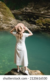 A Beautiful Woman In A White Long Dress And Hat Is Standing By The Water And Smiling. Travel Concept.