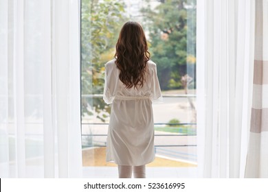 Beautiful Woman In White Silk Robe Standing Near Window