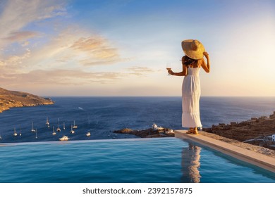 A beautiful woman in white summer dress by the swimming pool enjoys the sunset with a glass of wine - Powered by Shutterstock