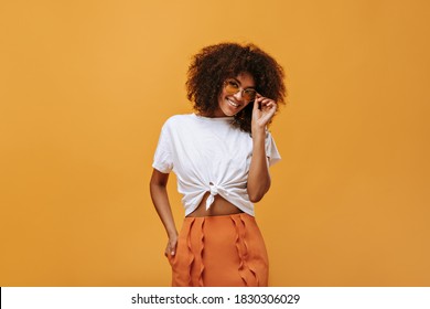 Beautiful woman in white t-shirt smiles on yellow background. Trendy girl with wavy hair in sunglasses poses on isolated backdrop.. - Powered by Shutterstock