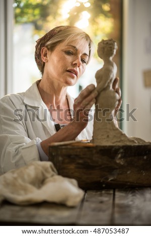 Beautiful woman who makes sculpture with a lap. she is in her atelier. , she is concentrated, she is sculpting a woman . the statue is at foreground. there is a view on garden at background.
