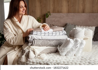 Beautiful Woman In Winter Thick Warm Robe Is Sitting And Neatly Folding Bed Linens And White Bath Towels. Organizing And Sorting Clean Laundry. Organic And Natural Cotton Textile. Manufacture.