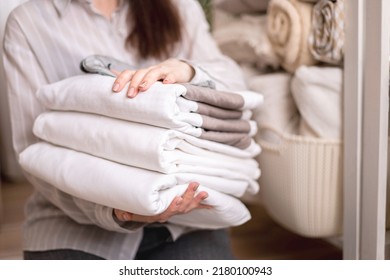 Beautiful woman in winter thick warm robe is sitting and neatly folding bed linens and white bath towels. Organizing and sorting clean laundry. Organic and natural cotton textile. Manufacture. - Shutterstock ID 2180100943