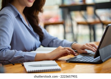 A beautiful woman working at a coffee shop with a computer, phone, tablet at a coffee shop in the morning with a cheerful mood and smiling. - Shutterstock ID 2223657901