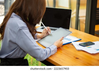 A beautiful woman working at a coffee shop with a computer, phone, tablet at a coffee shop in the morning with a cheerful mood and smiling. - Shutterstock ID 2223657903