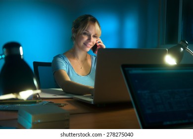 Beautiful woman working as interior designer, staying late at night in office with drawings and laptop computer to complete a project. The girl talks on mobile phone.   - Powered by Shutterstock