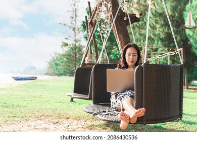 Beautiful woman working laptop while sitting in hammock on the beach