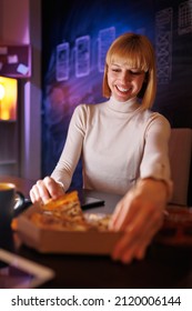 Beautiful Woman Working Late At Night, Sitting At Her Desk In An Office And Eating Pizza