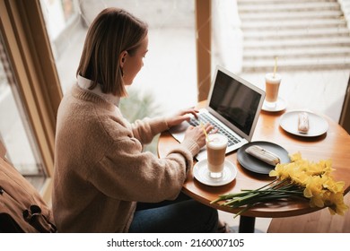 A Beautiful Woman Works Remotely In A Bright Cozy Cafe On A Laptop With A Cup Of Coffee.