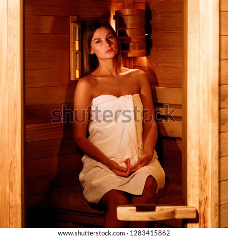 Beautiful woman wrapped in white towel takes a wooden sauna. Relax, vacation, wellness center concept.