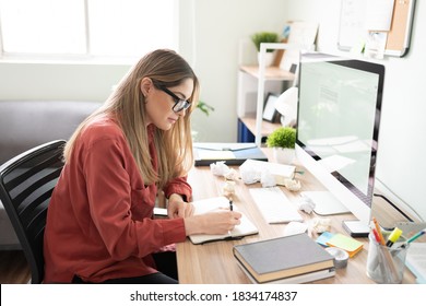 Beautiful woman and writer taking some notes in a notepad and filling the desk with crumpled paged due to her lack of inspiration - Powered by Shutterstock