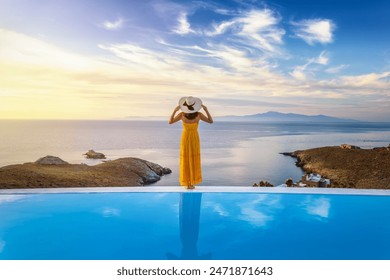 A beautiful woman in yellow summer dress by the swimming pool enjoys the sunset over the mediterranean sea, Cyclades, Greece - Powered by Shutterstock