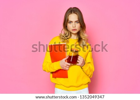 Beautiful woman in a yellow sweater. I have a red folder for papers and a drink a pink background