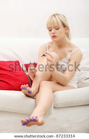 Beautiful woman's painting her nails. Sitting on couch. Indoor.