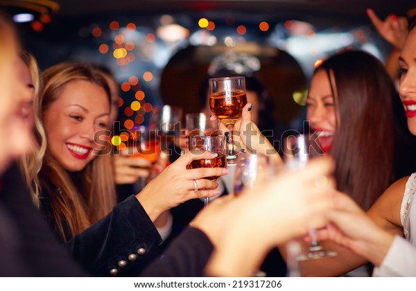 beautiful women clinking glasses in limousine.\
focus on glasses