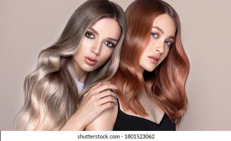Beautiful women with curly hair.Two pretty girls with hair coloring in red and  shatush techniques. Stylish hairstyle curls done in a beauty salon. Fashion, cosmetics and makeup.
