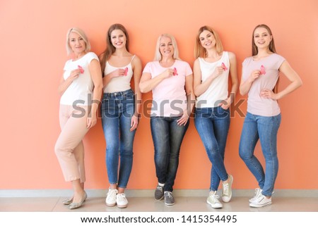 Beautiful women of different ages with pink ribbons near color wall. Breast cancer concept